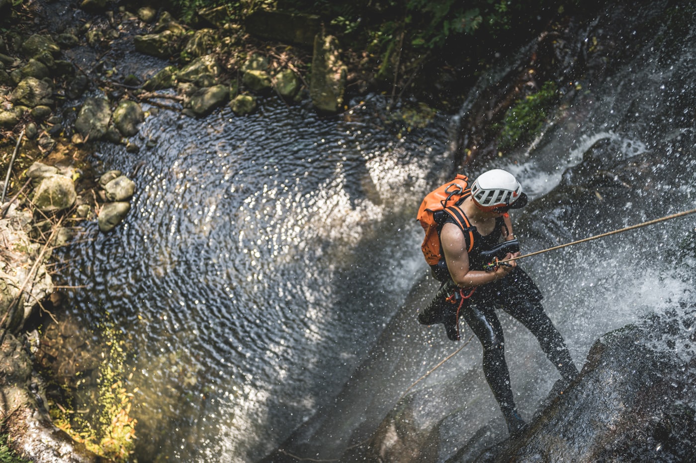 Canyoniste casqué en rappel dans une cascade, au-dessus d'une vasque d'eau claire