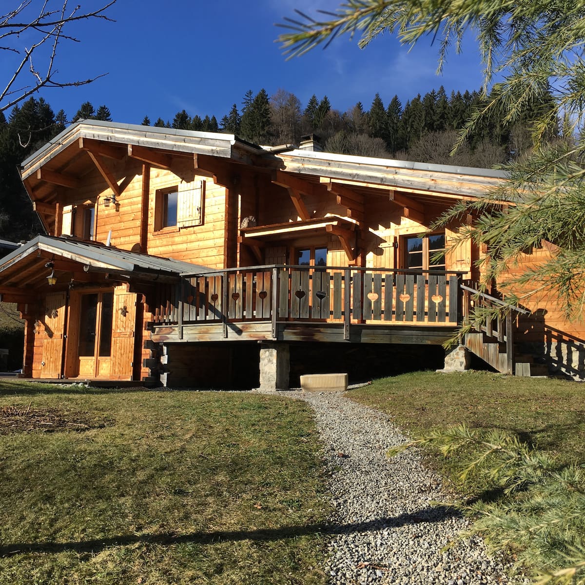 Le chalet À la maison en madriers de bois sous le soleil, terrasse aux balustres à cœurs