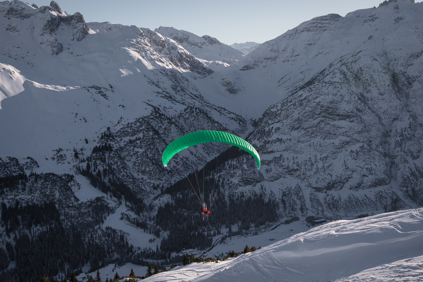 Parapente en vol au-dessus d'une vallée alpine enneigée, face aux sommets