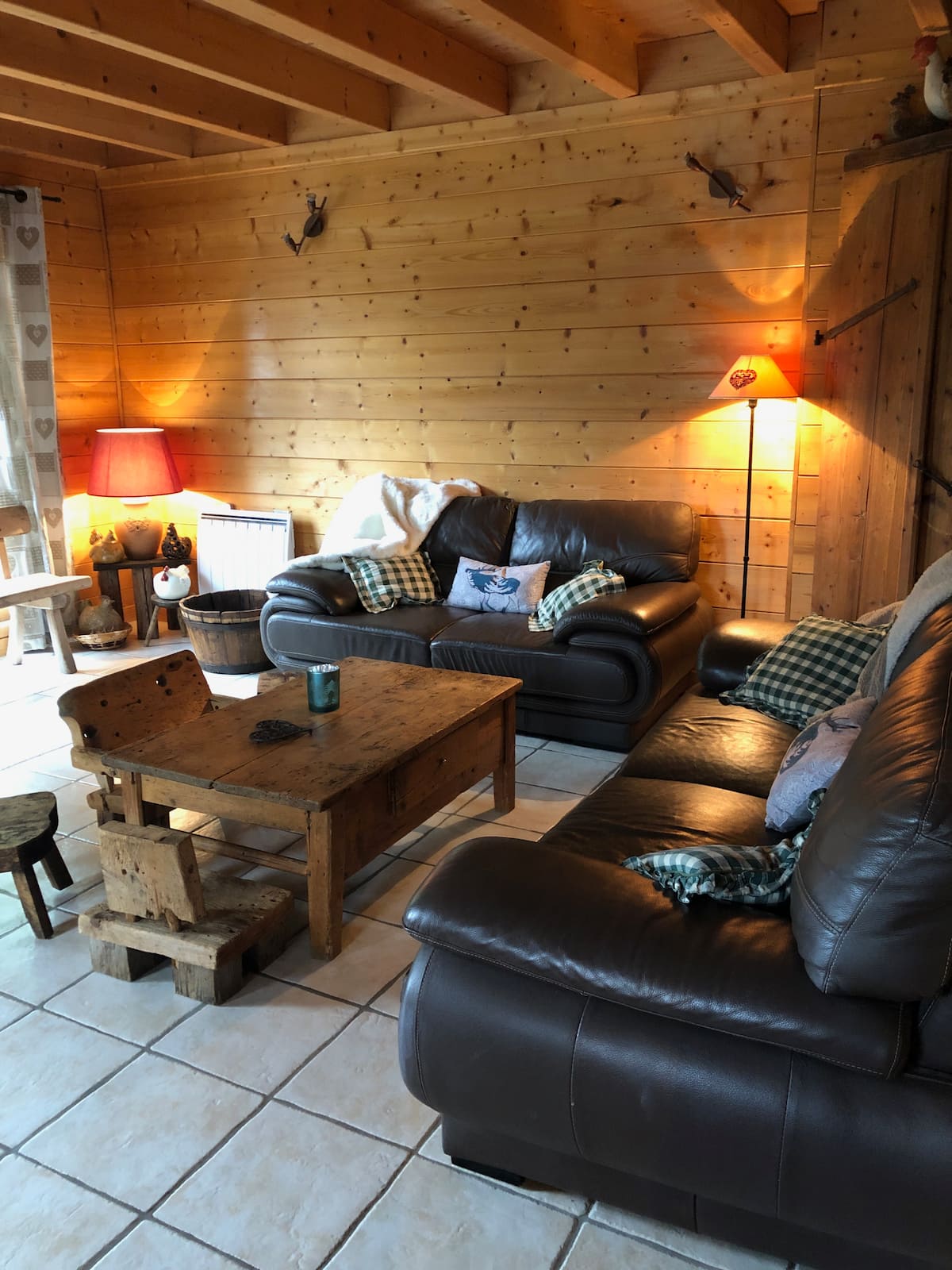 Le salon du chalet : canapés en cuir, plaids et lumières chaudes sur les murs en madriers